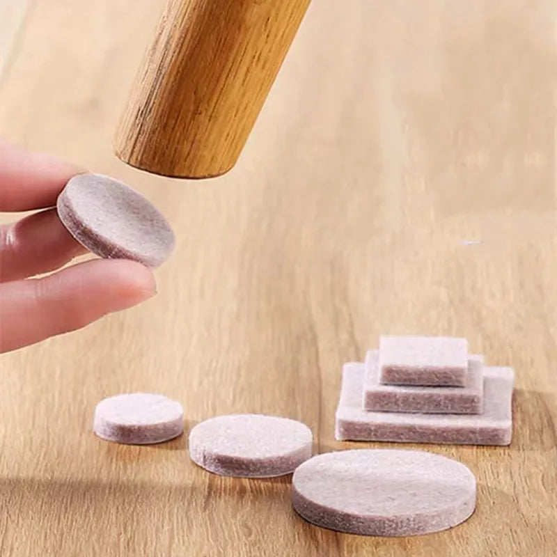 Felt furniture pads on a wooden surface with a hand holding one pad.